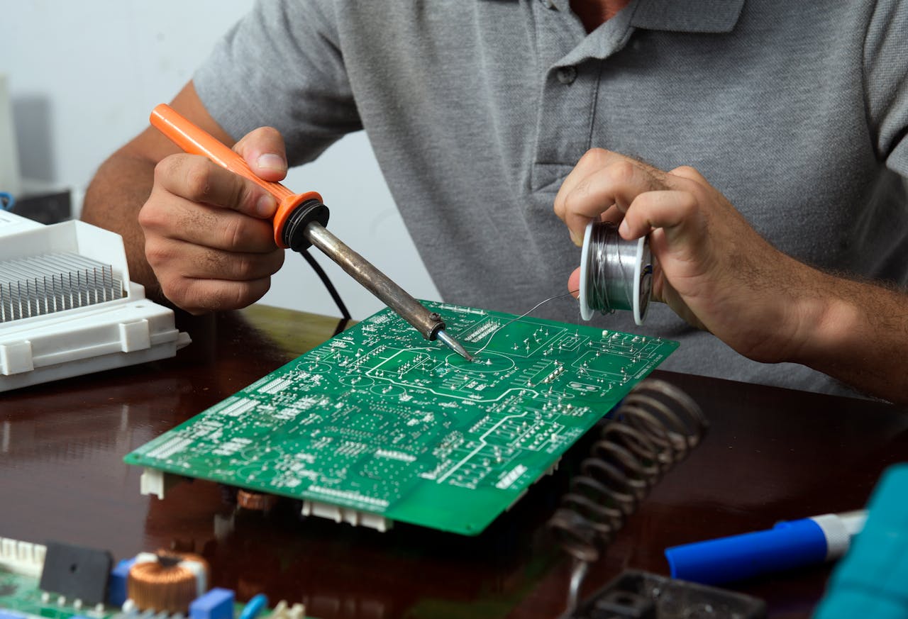 Close-up of a technician soldering a circuit board in an electronics workshop.