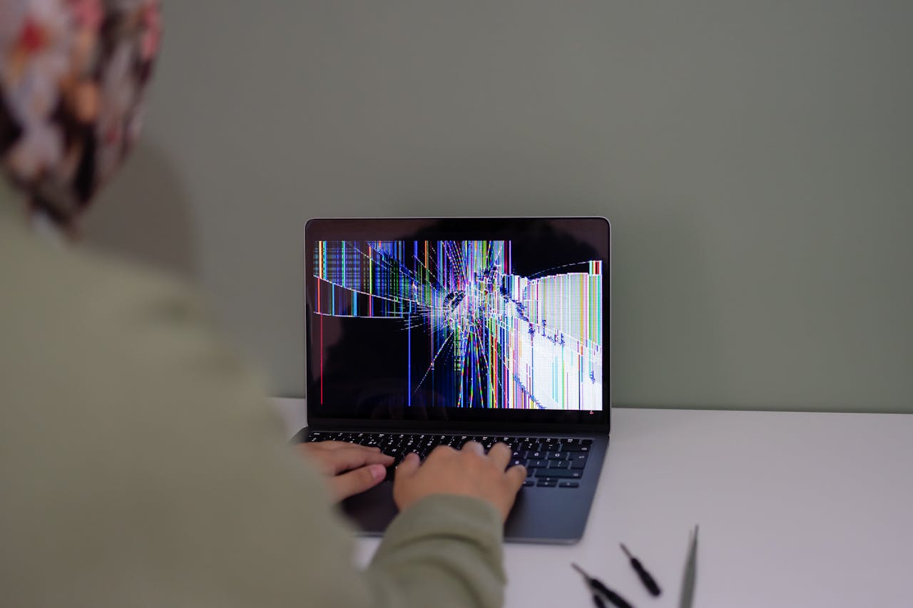 Adult working on a laptop with a cracked screen, indoors setting.